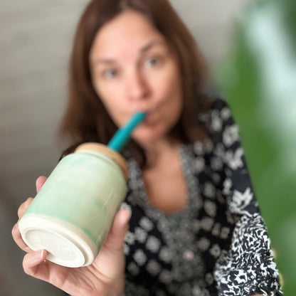 Person holding a green and white cup with a straw, blurred background