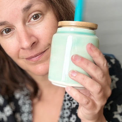 Woman holding a light green ceramic cup with a wooden lid and blue straw.