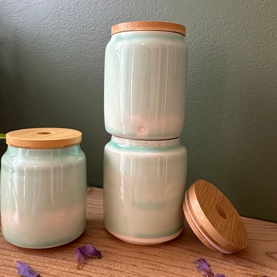 Three ceramic jars with wooden lids on a wooden surface against a gray wall.