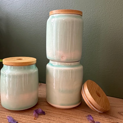 Three ceramic jars with wooden lids on a wooden surface against a gray wall.