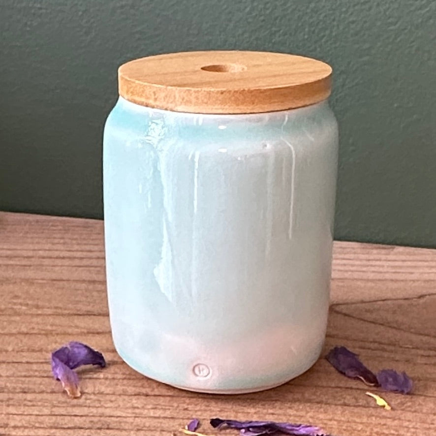 White ceramic diffuser with a wooden lid on a wooden surface with purple flowers.