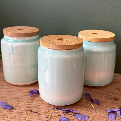 Three glass jars with wooden lids on a wooden surface with dried flowers.