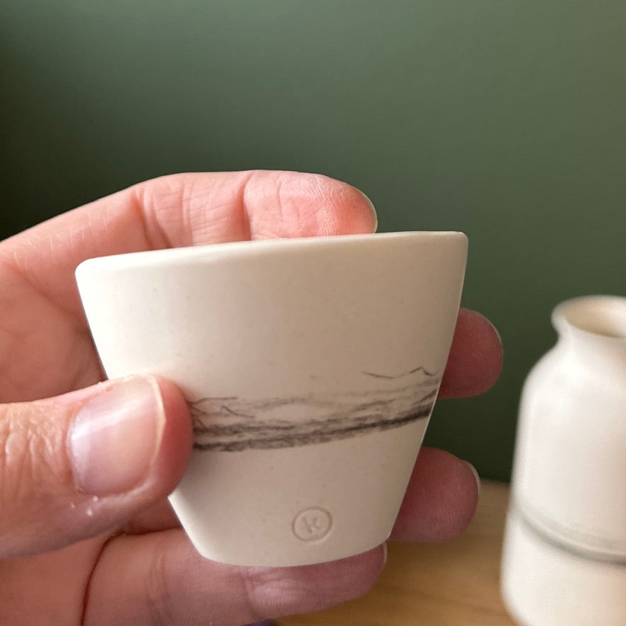 Hand holding a small white ceramic cup with marbled design against a green background