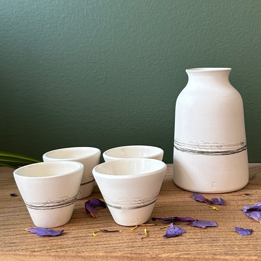 Set of white ceramic cups and a vase on a wooden surface with a green wall background.