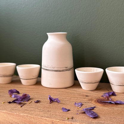 Set of ceramic vases and bowls on a wooden surface with purple flowers against a green wall.