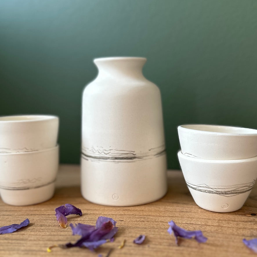 Set of white ceramic vases and bowls on a wooden surface with a green background