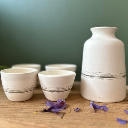 Set of ceramic cups and a bottle on a wooden surface with a green background