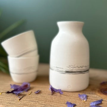 White ceramic diffuser on a wooden surface with small purple flowers around it, against a green background.
