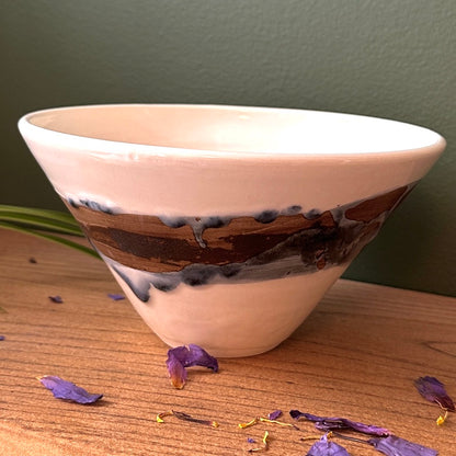 Ceramic bowl with brown and black design on a wooden surface with dried flowers.