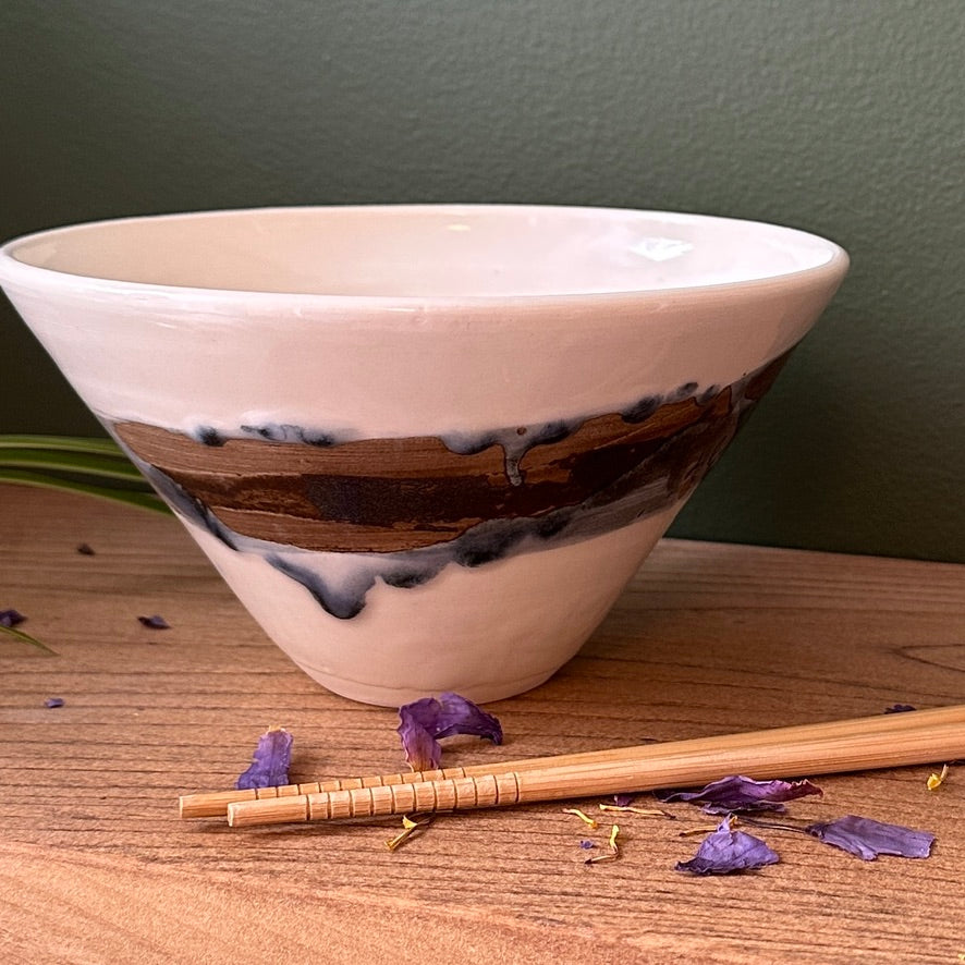 Ceramic bowl with wooden accent on a wooden surface with purple flowers and chopsticks.