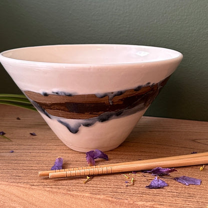 Ceramic bowl with wooden accent on a wooden surface with purple flowers and chopsticks.